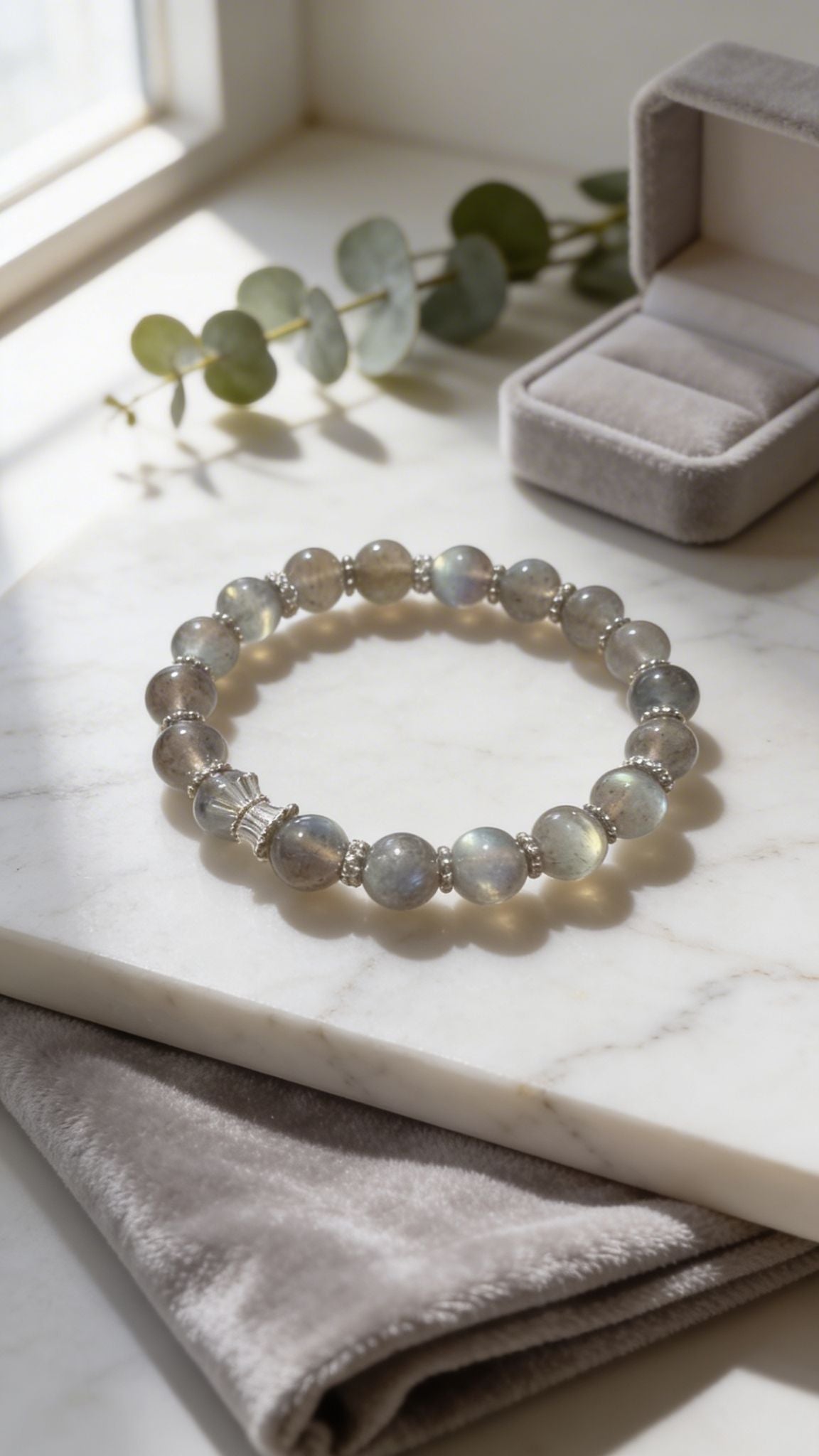 Labradorite Bracelet on a marble surface with eucalyptus leaves and a jewelry box in the background